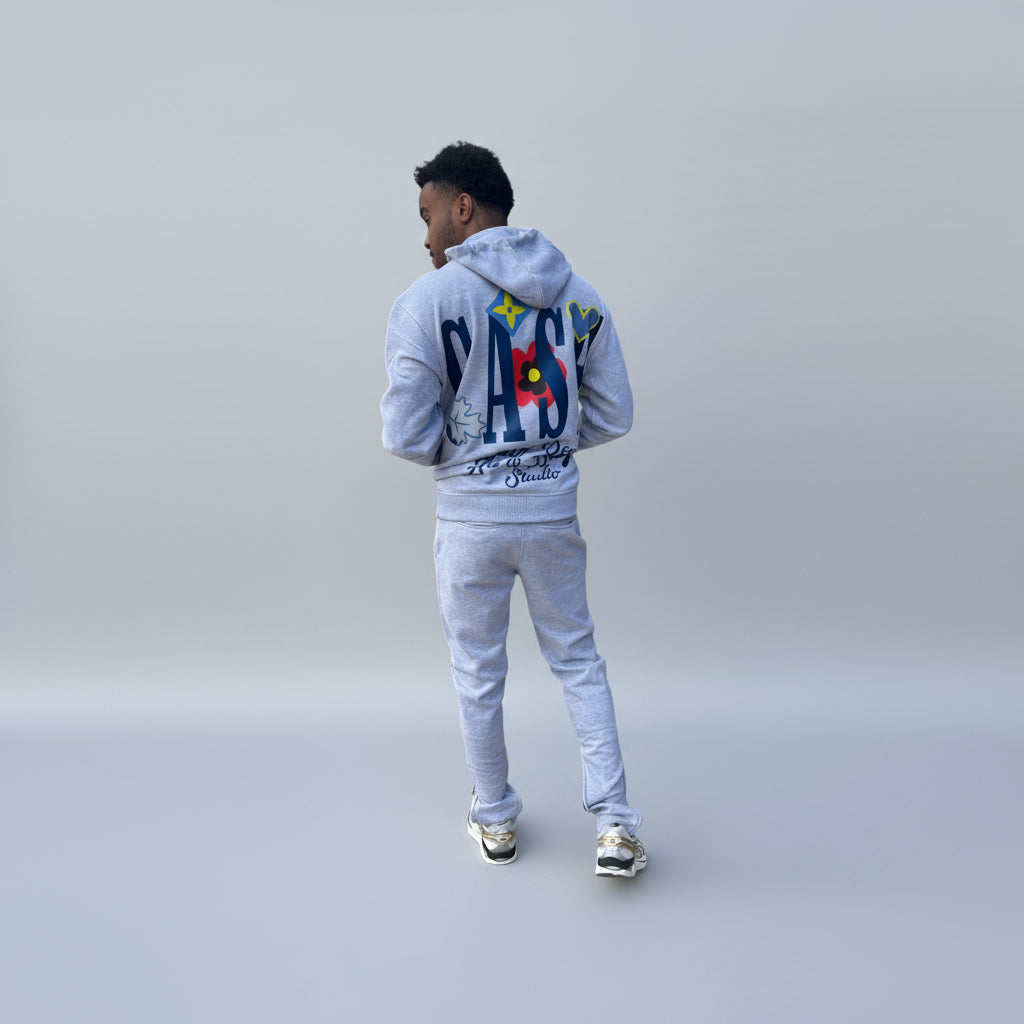 Person wearing a gray hoodie and pants with a colorful design on the back, standing against a white background.